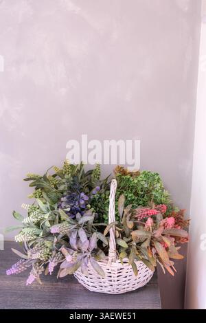 Ein Korb mit Blumen mit weißem Griff sitzt auf einem Tisch. Die Blumen sind eine Mischung aus verschiedenen Farben und Arten, die eine lebendige und lebhafte Atmosphäre schaffen Stockfoto