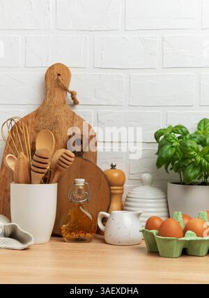 Rustikale Küchenszene mit Holzutensilien, frischen Eiern, Basilikumpflanzen und verschiedenen Kochzutaten für eine gemütliche und einladende Atmosphäre Stockfoto