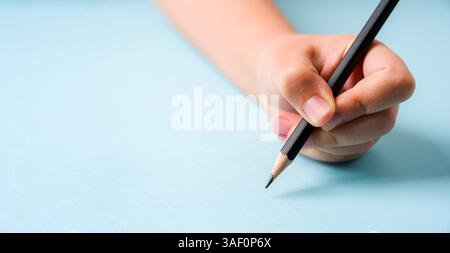 Die linke Hand hält einen Kugelschreiber auf einem offenen Notizbuch auf blauem Hintergrund Stockfoto