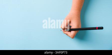 Die linke Hand hält einen Kugelschreiber auf einem offenen Notizbuch auf blauem Hintergrund Stockfoto