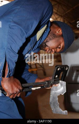 April 2005; Al Asad, Irak; KAYSON S. WILLIAMS, ein Hubschraubermechaniker aus San Diego, Kalifornien, mit dem taktischen Nachhaltigkeitsprüfungsteam von Bell Aerospace Services, Inc., stanzt am 20. April Schraubenlöcher auf ein Metallblech, während er eine Starterreichweite für eine AH-1W Super Cobra herstellt. Die Schutzvorrichtung verhindert, dass Wasser und Sand in den Anlasser gelangen. Obligatorischer Ausweis: Foto von Sgt. Juan Vara/DOD/ZUMA Press. (©) Copyright 2005 by US DOD Photo Stockfoto
