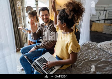 Glücklicher Vater im Rollstuhl mit interrassischen Töchtern mit Laptop zusammen, Bildung, lustiges Konzept Stockfoto