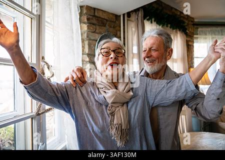 Fröhlich aktiv alt pensioniert romantisches Seniorenpaar tanzt lachend und hat Spaß im Wohnzimmer Stockfoto