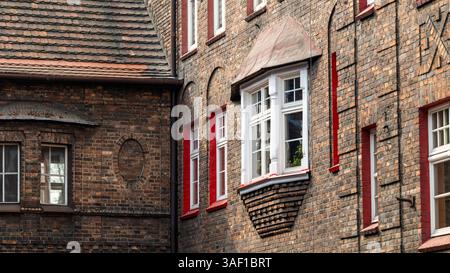 Ziegelfassade eines Mietshauses in einem Arbeiterwohnheim. Wunderschöne Fensterdetails. Weiße Fensterrahmen. Bay-Fenster. Historische Wohnsiedlung Katow Stockfoto