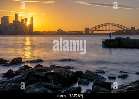 Ein Mann fischt im Wasser in der Nähe einer Brücke. Die Sonne untergeht im Hintergrund und strahlt ein warmes Leuchten über die Szene. Stockfoto
