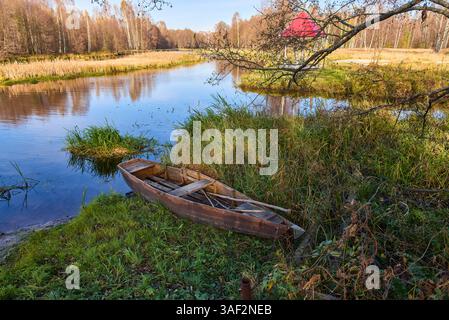 Eine ruhige Seeszene mit einem Pavillon mit rotem Dach, umgeben von Herbstbäumen und einem Holzboot am grasbewachsenen Ufer Stockfoto