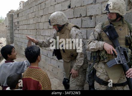 9. März 2005; Fallujah, Irak; Marinestützpunkt MATTHEW S. WEEMS, 33 Jahre alter Kaplan für das 3. Bataillon, 4. Marines, Regimentskampfteam 1, gibt einem irakischen Jungen fünf, als Petty Officer 2. Klasse AARON G. NEELY, 21-jähriger Religionsprogrammspezialist für das Bataillon, Sicherheit während einer Patrouille durch Fallujah, Irak, 9. März. Weems und Neely nehmen an vielen verschiedenen Aspekten der Operationen des Bataillons Teil, um eine Präsenz unter den Marines zu erhalten. Stockfoto