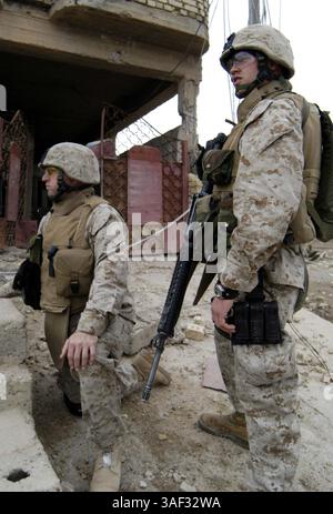 9. März 2005; Fallujah, Irak; Marinestützpunkt MATTHEW S. WEEMS, 33-jähriger Kaplan für das 3. Bataillon, 4. Marines, Regimentskampfteam 1, kniet als Petty Officer 2. Klasse AARON G. NEELY, 21-jähriger Spezialist für religiöse Programme für das Bataillon, Sicherheit während einer Patrouille durch die Stadt Fallujah im Irak am 9. März. Weems und Neely nehmen an vielen verschiedenen Aspekten der Operationen des Bataillons Teil, um eine Präsenz unter den Marines zu erhalten. Stockfoto