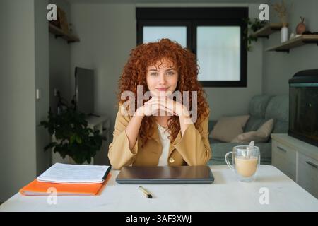 Junge Geschäftsfrau, die am Schreibtisch sitzt und in die Kamera lächelt Stockfoto