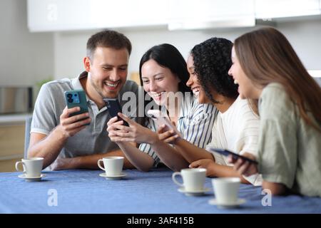 Glückliche Gruppe von Freunden, die ihre Handys in der Küche zu Hause checken Stockfoto