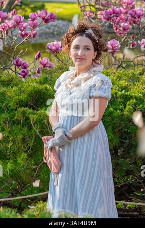 Eine Frau im Stil des 19. Jahrhunderts, umgeben von Frühlingsblüte und grüner Landschaft Stockfoto