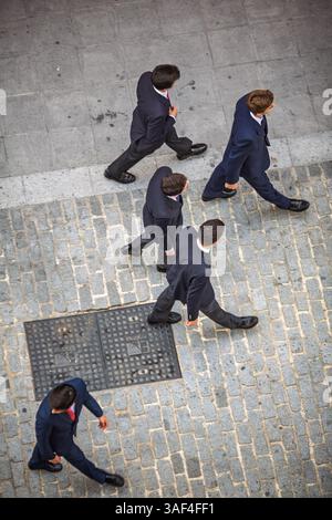 Junge Männer in Anzügen, die während der Karwoche in Sevilla auf Kopfsteinpflasterstraßen laufen. Stockfoto