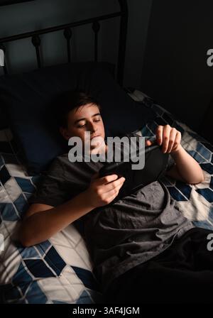 Teenager im Schlafzimmer, der etwas auf dem ipad-Tablet auf seinem Bett sieht. Stockfoto