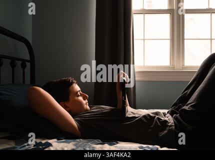 Teenager im Schlafzimmer, der etwas auf dem ipad-Tablet auf seinem Bett sieht. Stockfoto