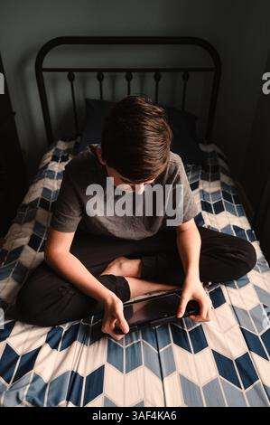 Teenager im Schlafzimmer, der etwas auf dem ipad-Tablet auf seinem Bett sieht. Stockfoto