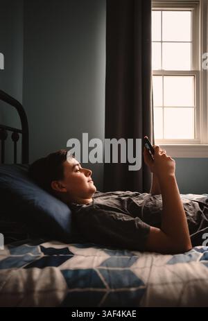 Teenager im Schlafzimmer mit Smartphone, während er auf seinem Bett lag. Stockfoto