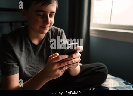 Nahaufnahme eines Teenager-Jungen im Schlafzimmer mit Smartphone auf seinem Bett. Stockfoto