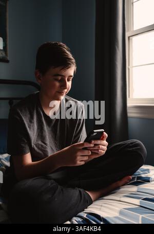 Nahaufnahme eines Teenager-Jungen im Schlafzimmer mit Smartphone auf seinem Bett. Stockfoto