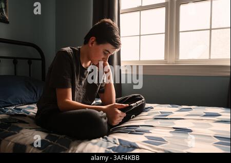 Teenager im Schlafzimmer, der etwas auf dem ipad-Tablet auf seinem Bett sieht. Stockfoto