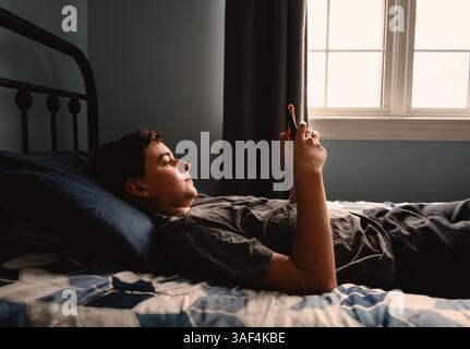 Teenager im Schlafzimmer mit Smartphone, während er auf seinem Bett lag. Stockfoto