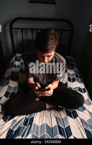 Großer Winkel eines Teenager-Jungen im Schlafzimmer mit Smartphone auf seinem Bett. Stockfoto