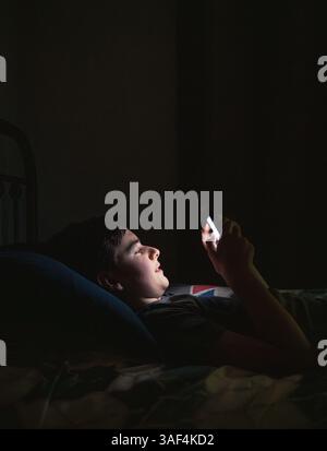 Teenager im Schlafzimmer mit Smartphone, während er nachts auf seinem Bett lag. Stockfoto