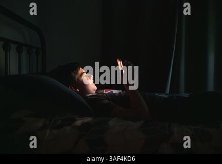 Teenager im Schlafzimmer mit Smartphone, während er nachts auf seinem Bett lag. Stockfoto