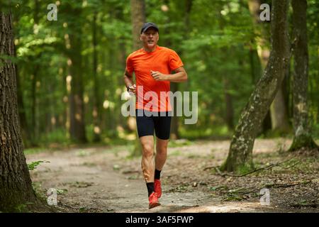 Ein Mann mittleren Alters läuft auf Waldwegen in leuchtend orangefarbenem Shirt und sportlicher Ausrüstung Stockfoto