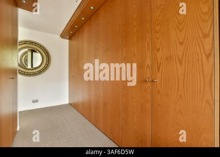 Ein eleganter Korridor mit Holzschiebetüren, moderner Einrichtung und rundem Spiegel, der eine stilvolle Inneneinrichtung unterstreicht. Stockfoto