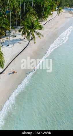Erleben Sie die ruhige Schönheit der Insel Koh Kood in Thailand, wo weicher weißer Sand auf klares türkisfarbenes Wasser trifft. Palmen schwanken sanft, während Strandgäste einen friedlichen Tag unter der Sonne genießen. Stockfoto