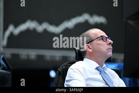 07. April 2025, Hessen, Frankfurt/Main: Während ein Händler auf der Börse der Frankfurter Wertpapierbörse seine Monitore beobachtet, ist im Hintergrund die Anzeigetafel mit der Dax-Kurve zu sehen. Zu Beginn der neuen Handelswoche sank der deutsche Aktienindex (Dax) um rund zehn Prozent. Foto: Arne Dedert/dpa Stockfoto