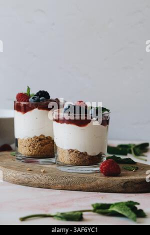 Kleinigkeiten, Parfait oder Käsekuchen auf Gläsern, Schichten Crumble Cookies, weiße Creme, Erdbeermarmelade und Beeren auf Minzblättern. Stockfoto