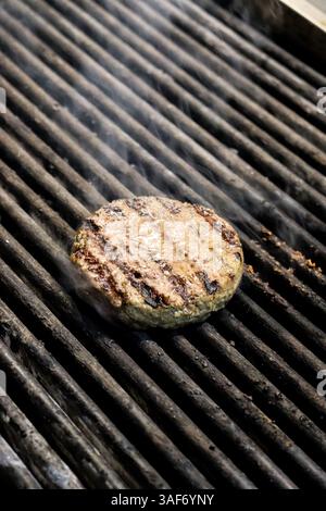 Klassischer Hamburger patti auf einem Grill, der mit Rauch gegrillt wird Stockfoto