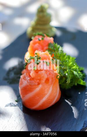 Lachs-Sushi-Maki-Rollen, dekoriert mit Kräutern und Wasabi, auf einem flachen dunklen Teller oder Tablett, auf weißem Hintergrund. Sommerlicht, Schatten. Mittagsstimmung oder earl Stockfoto