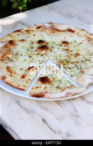 Ganze Pizza und ein geschnittenes Stück margherita oder weiße Pizza, auf einem marmorfarbenen Hintergrund. Sommerlicht, Mittagsstimmung Stockfoto