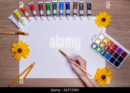 Arbeitsbereich des Künstlers mit Tuben und leerer Leinwand. Ein kreativer Arbeitsbereich mit leerer weißer Leinwand, umgeben von leuchtenden Farbröhren Stockfoto