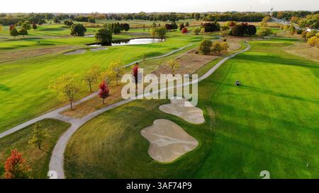 Blick aus der Vogelperspektive auf den malerischen Golfplatz im Herbst. Aus der Vogelperspektive auf einen grünen Golfplatz mit Sandbunkern, Wegen, Bäumen in Herbstfarben und einem Teich im Stockfoto