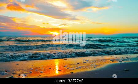 Atemberaubender Sonnenuntergang über den Meereswellen. Ein faszinierender Blick auf den Sonnenuntergang über einem ruhigen Ozean mit farbenfrohen Himmel, der sich auf dem Wasser spiegelt. Stockfoto