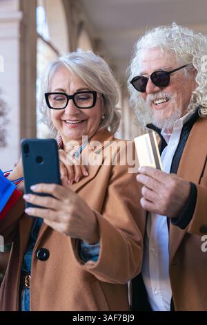 Kaukasisches Seniorenpaar, das im Freien mit Smartphone und Kreditkarte einkaufen kann Stockfoto