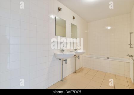Ein modernes Bad mit klaren Linien, weißen Fliesen, zwei Waschbecken und Badewanne schafft eine minimalistische und geräumige Atmosphäre. Stockfoto