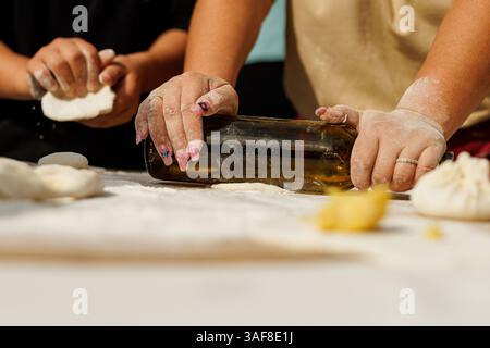 Die Hausfrau rollt den Teig mit einer Weinflasche aus Stockfoto