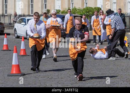 Bath, UK. April 2025. Während der Wettkampf heiß wird, fällt einer der Kellner beim Wagenrennen vor dem Royal Crescent zu Boden. Kellner aus Restaurants in Bath mit Getränketabletts und Baths berühmten Sally Lunn Brötchen werden auf den Bildern abgebildet, während sie sich auf dem berühmten Royal Crescent in Bath gegenseitig rasen. Das Kellnerrennen startet die Bath Restaurantwoche, die vom 3. Bis 11. Mai 2025 stattfindet. 31 Kellner nahmen am Rennen Teil und der berühmte lokale Baker Richard Bertinet überreichte die Preise an die Gewinner. Jedes Team, das am Rennen teilnahm, war Spendensammlung für Hospitality Stockfoto