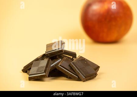Stapel Schokoladenriegel mit rotem Apfel im Hintergrund auf cremefarbenem Hintergrund Stockfoto