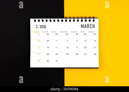 Schreibtischkalender März 2026 auf schwarzem und gelbem Hintergrund, Flat Lay. Stockfoto