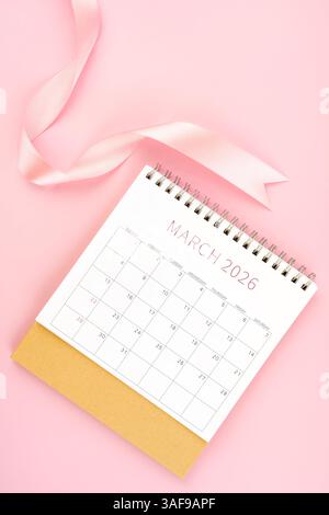 März 2026 Schreibtischkalender mit rosa Farbband, Flat Lay. Stockfoto