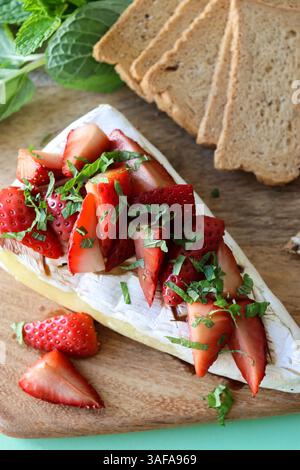 Blick von oben auf einen gebackenen Brie-Käse mit Erdbeeren auf einem Holzbrett, serviert mit Crackern Stockfoto