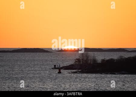 Die helle orange Sonne untergeht während des Sonnenuntergangs hinter dunklen Silhouetten von felsigen Inseln im Meer. Stockfoto