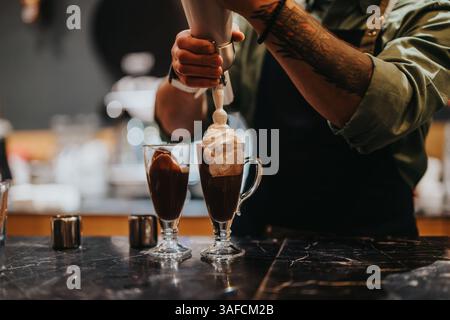 Barista bereitet heiße Schokolade mit Schlagsahne in Glasbechern zu Stockfoto