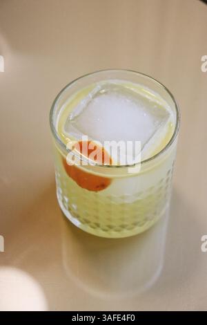 Eleganter Zitruscocktail mit Eiswürfel und Orangenschale in einem strukturierten Glas auf neutralem Hintergrund – Draufsicht Stockfoto