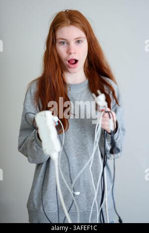 Teenager-Mädchen mit langen roten Haaren, schmutzige Drähte in beiden Händen, verwirrter Ausdruck Stockfoto